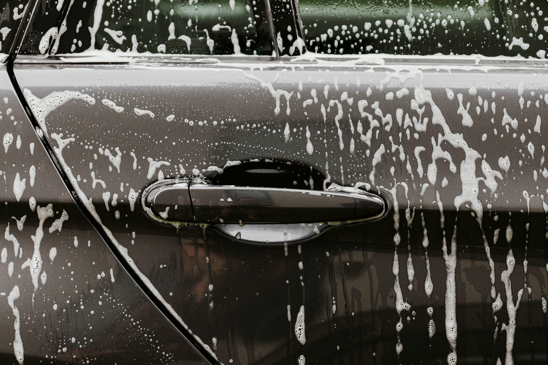 Detailed close-up of soap suds on a black car door during a wash, highlighting automotive care.