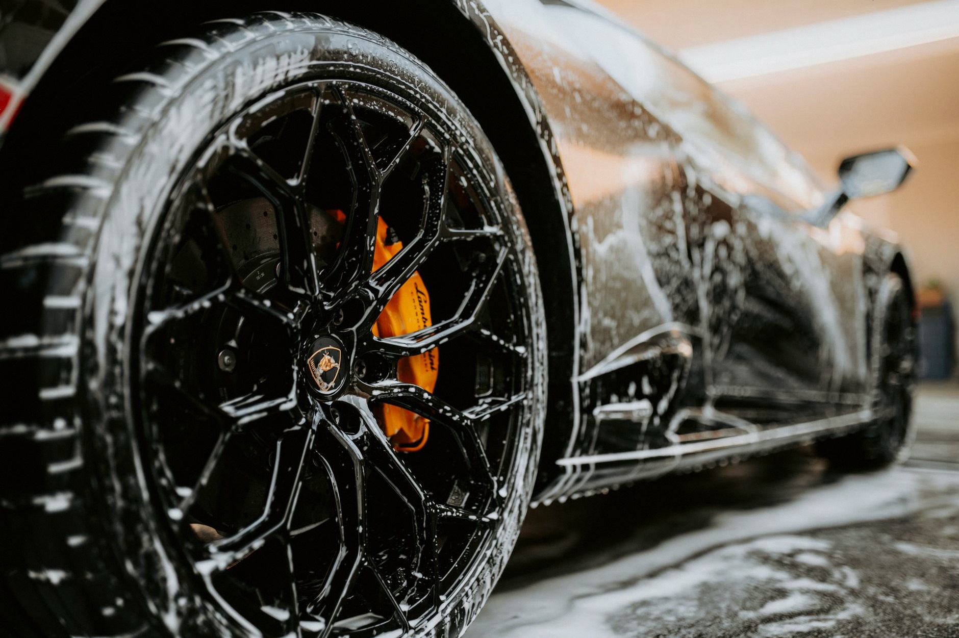 Detailed close-up of a luxury car wheel covered in soap suds during a professional car wash.